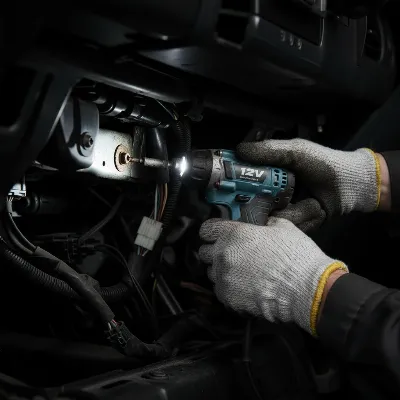 A 12V compact impact driver used by a technician in a very tight, dimly lit space, like under a car's dashboard or inside a small cabinet. The tool's small size and LED light are highlighted, showing ease of use in confined areas. Realistic, focused on the tool and hands.